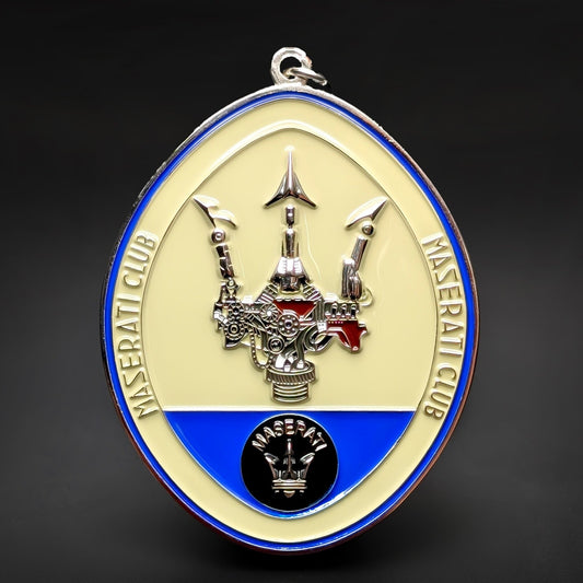 Double-sided oval metal Maserati Club badge keychain, cream face and blue ring reading MASERATI CLUB, a chrome trident over a silver-and-red engine, black MASERATI emblem below, chrome border and hanging loop.