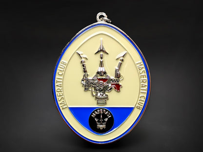Maserati Club badge keychain featuring a mechanical-style silver trident on a cream and blue oval enamel background.