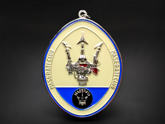 Maserati Club badge keychain featuring a mechanical-style silver trident on a cream and blue oval enamel background.