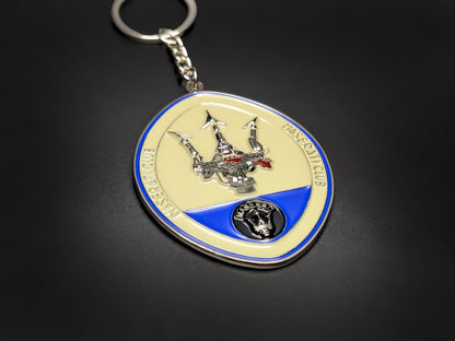 High-gloss Maserati car club badge keychain on a dark background, showing the polished silver metal and blue enamel trim.