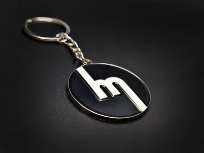 High-quality retro Mazda logo keychain on a dark background, showing the polished silver trim and durable metal chain.