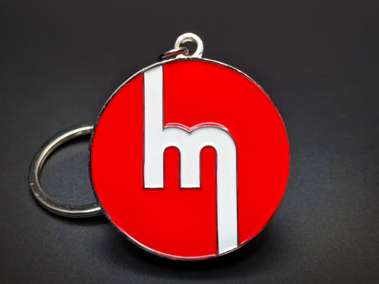 Vintage Mazda Miata badge keychain featuring the classic white block logo on a vibrant red enamel base.