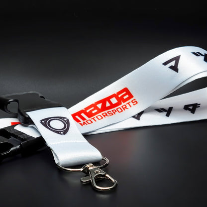 White Mazda lanyard with red Mazda Motorsports text and a black circular emblem, coiled with a black breakaway clip and silver clasp on a black surface.