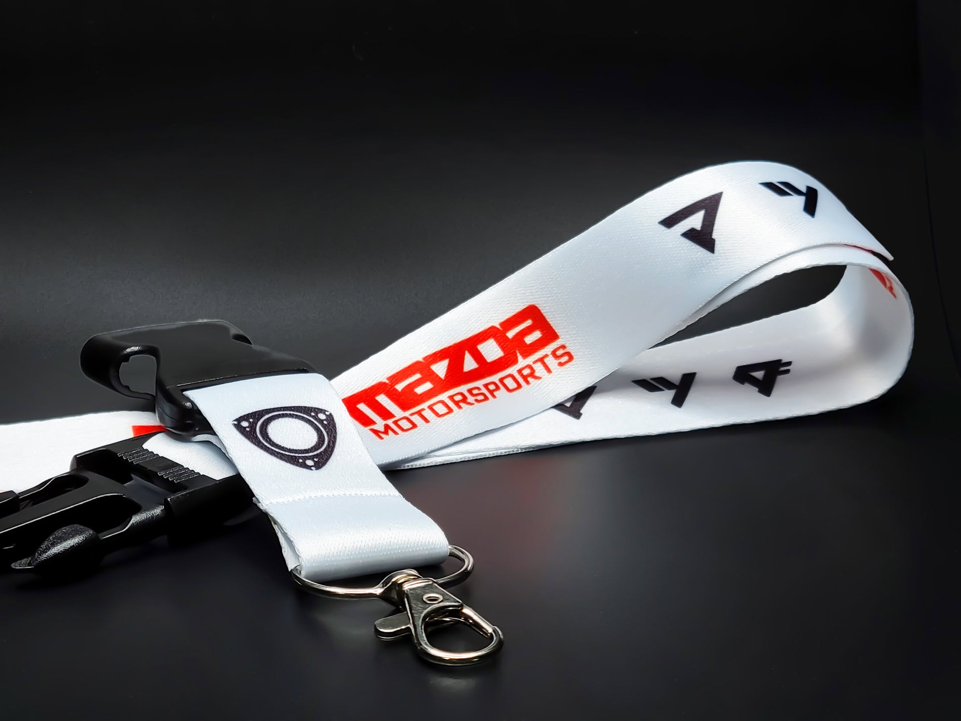 White Mazda Motorsports lanyard featuring a black rotary engine housing logo, red branding, and a silver lobster claw metal clasp.