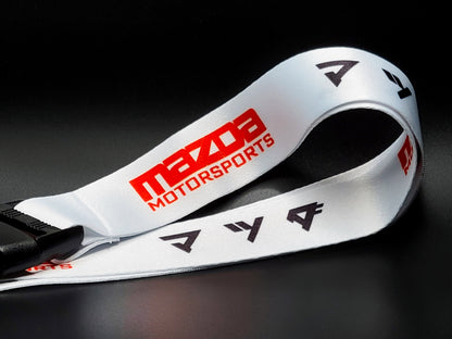 Close-up of a white satin Mazda lanyard showing the red Mazda Motorsports wordmark and repeating black Japanese katakana symbols.
