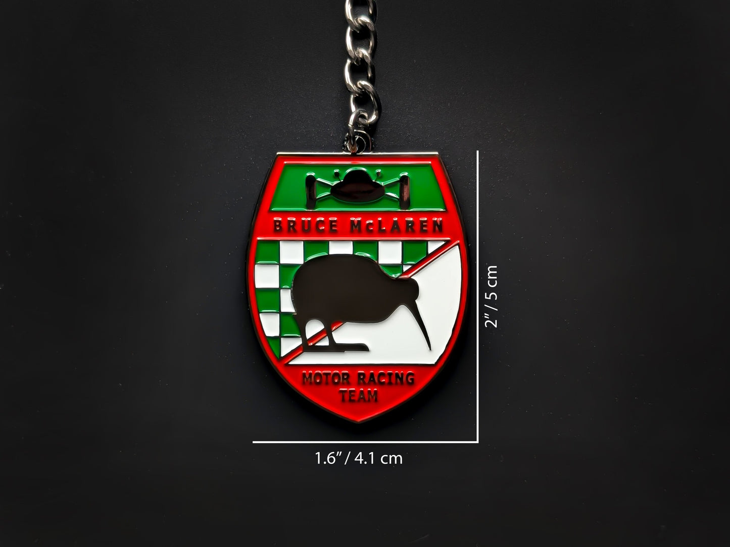 Dimension shot of the Bruce McLaren vintage badge keychain showing a size of 2 inches by 1.6 inches (5 cm by 4.1 cm).
