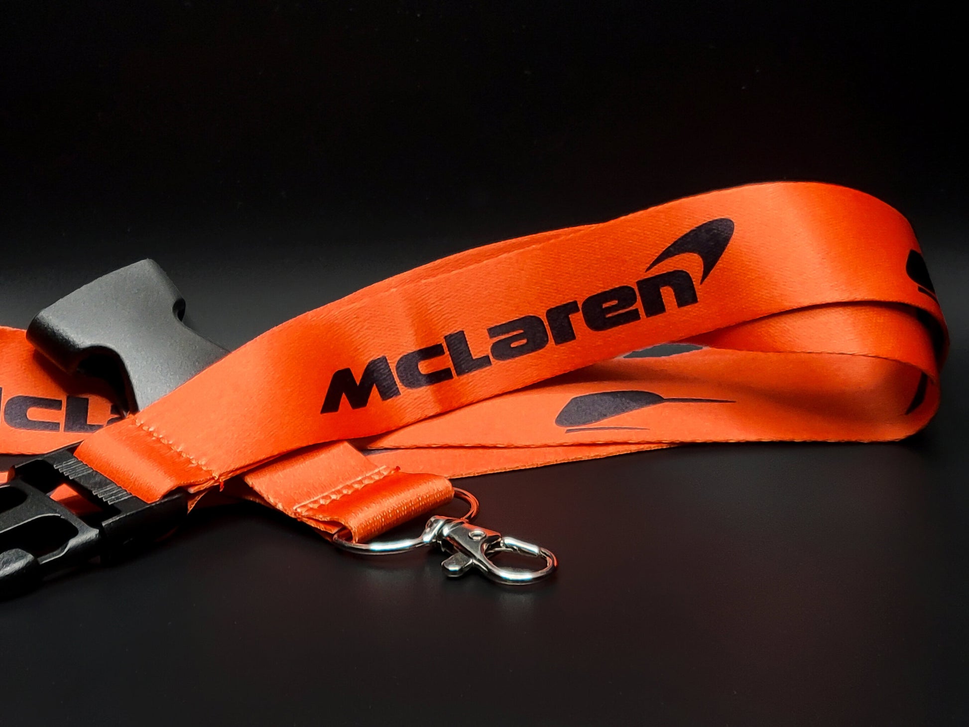 Bright orange McLaren lanyard with black McLaren text and the iconic Speedy Kiwi bird logo near a silver metal clasp.