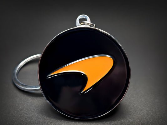 McLaren badge keychain featuring the Papaya Orange Speedmark logo on a circular high-gloss black enamel base.