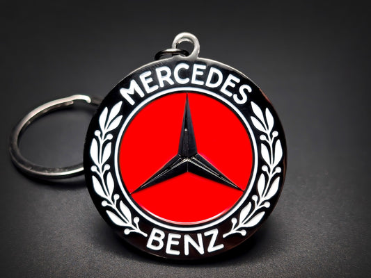Mercedes-Benz badge keychain featuring a black 3D star on a red enamel center, surrounded by white laurel wreaths and "Mercedes Benz" text.