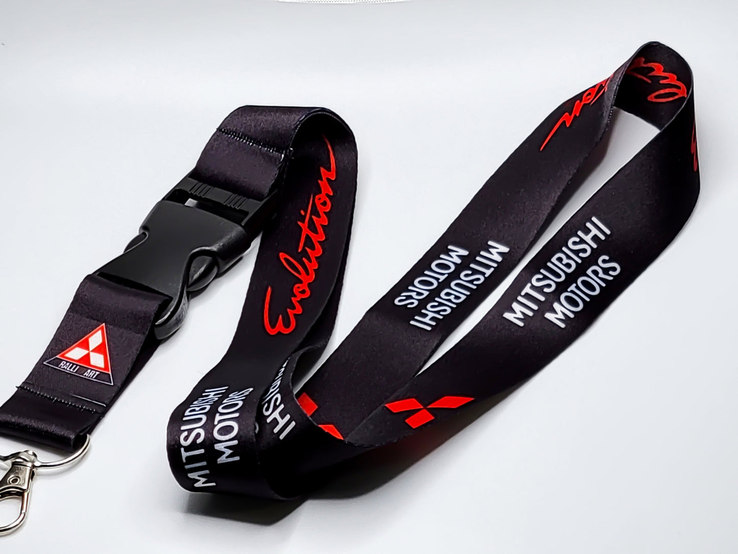 Premium black satin lanyard showcasing a repeating pattern of the red Evolution script, Mitsubishi Motors branding, and the Ralliart triangular logo.