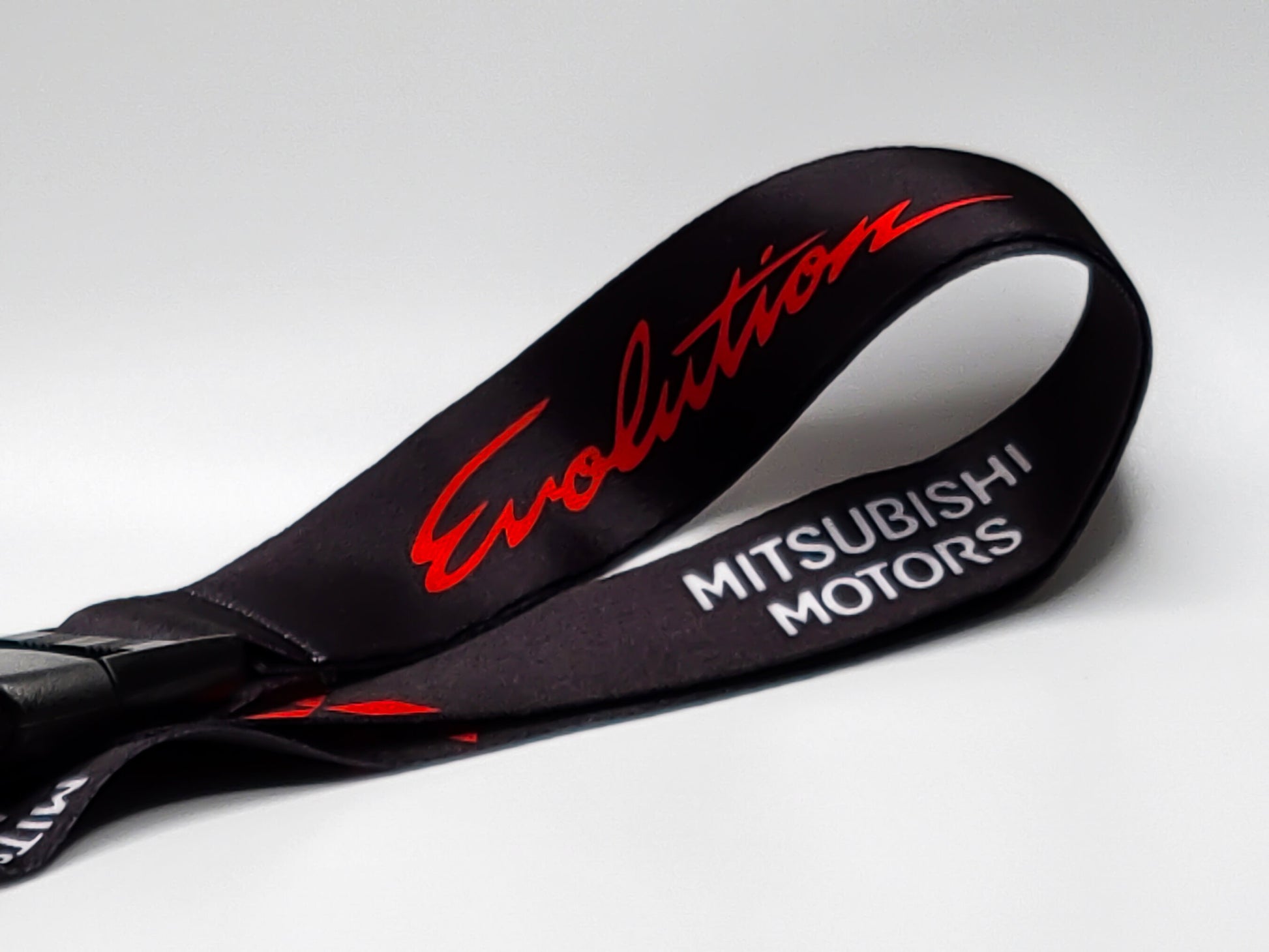 Close-up of a black automotive lanyard highlighting the vibrant red embossed Evolution script and white Mitsubishi Motors block lettering.
