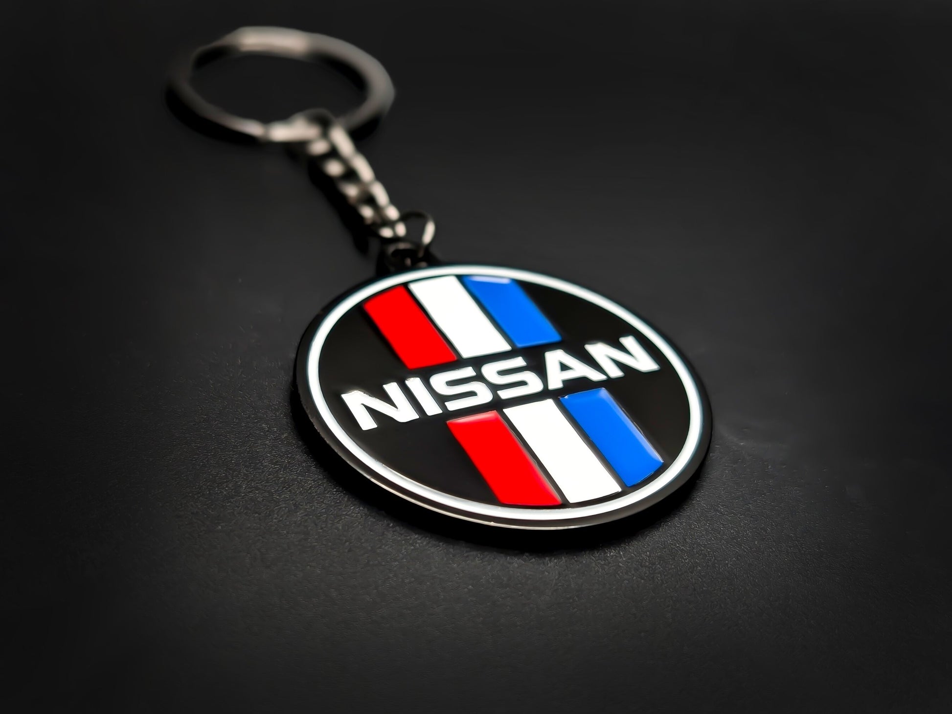 High-gloss Nissan retro competition stripes keychain on a dark background, showing the polished gunmetal chain and metallic rim.