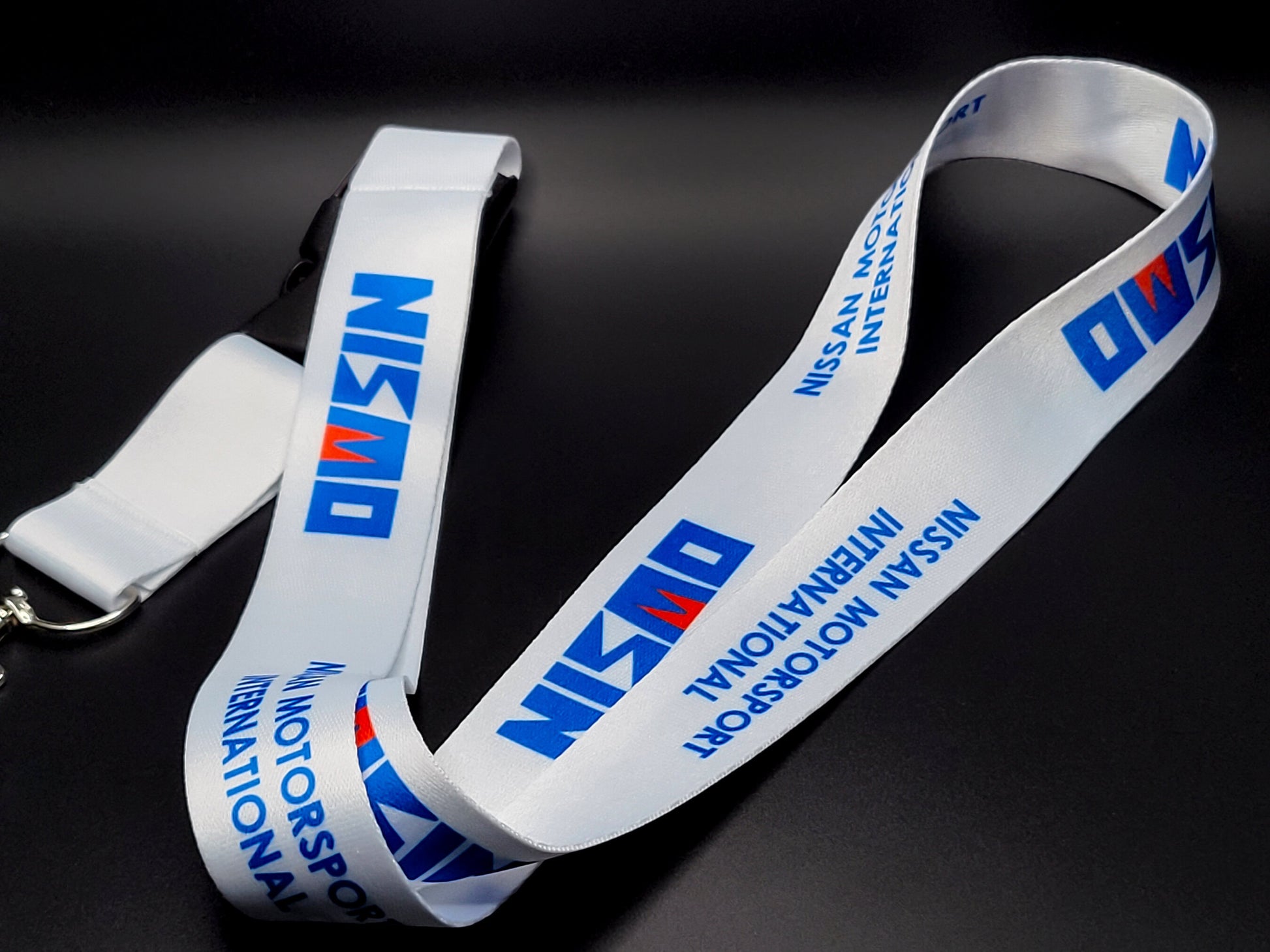 Premium white satin lanyard showcasing a repeating blue Nismo logo and "Nissan Motorsport International" wordmark.