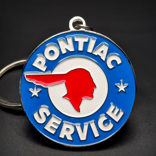 Double-sided metal Pontiac Service badge keychain, a blue medallion with a red chief-head emblem in a white circle, PONTIAC and SERVICE in white lettering, a star each side, dark surface.