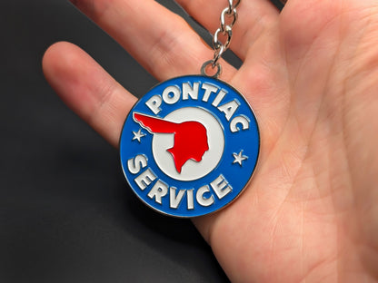 Circular Pontiac Service enamel badge keychain held in hand to demonstrate the premium metallic weight and vibrant color finish.