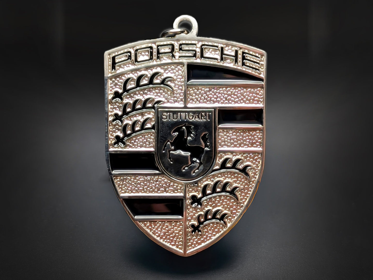 Porsche black badge keychain with silver 3D crest, black enamel stripes, and Stuttgart horse on a textured metallic shield.