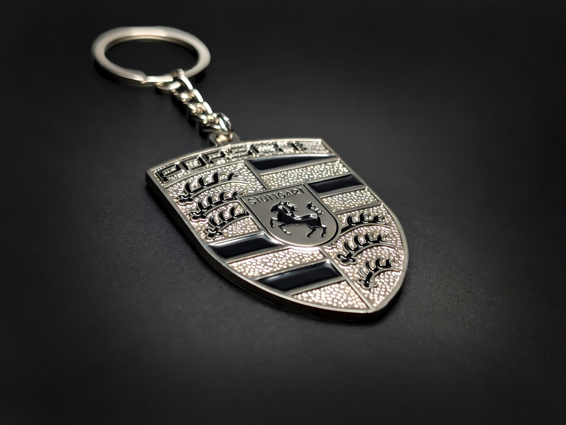 High-gloss black and silver Porsche crest keychain on a dark background, showcasing the polished metallic chain and rim.