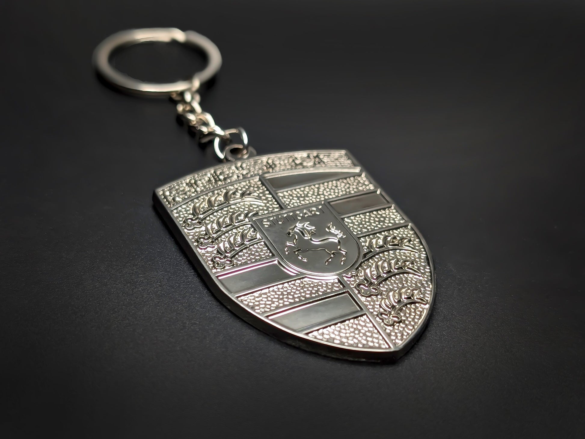 High-gloss Porsche silver metallic keychain on a dark background, showing the polished chrome rim and industrial steel-tone finish.