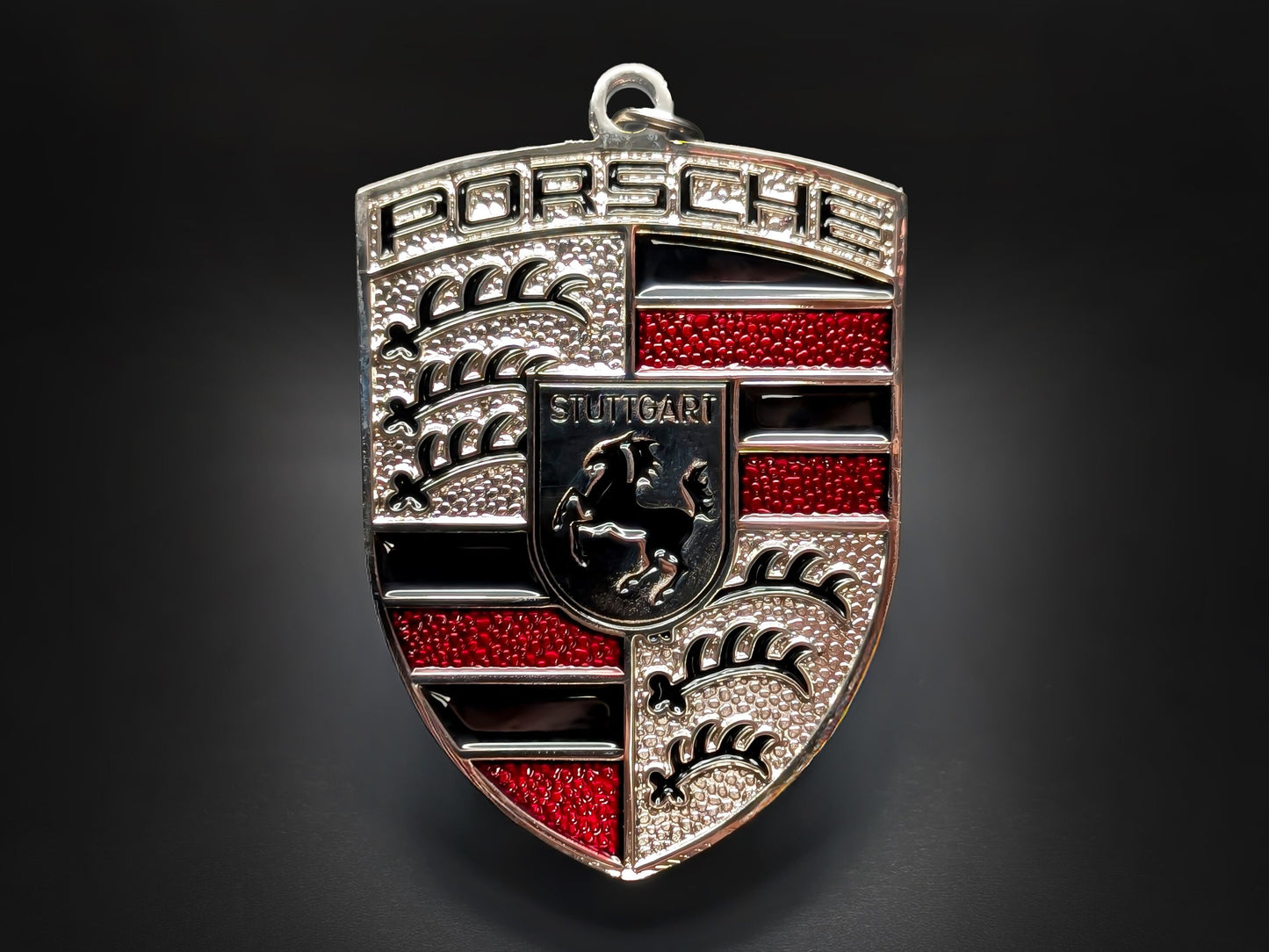 Porsche badge keychain featuring a textured red and silver crest with the Stuttgart horse and 3D embossed silver lettering.