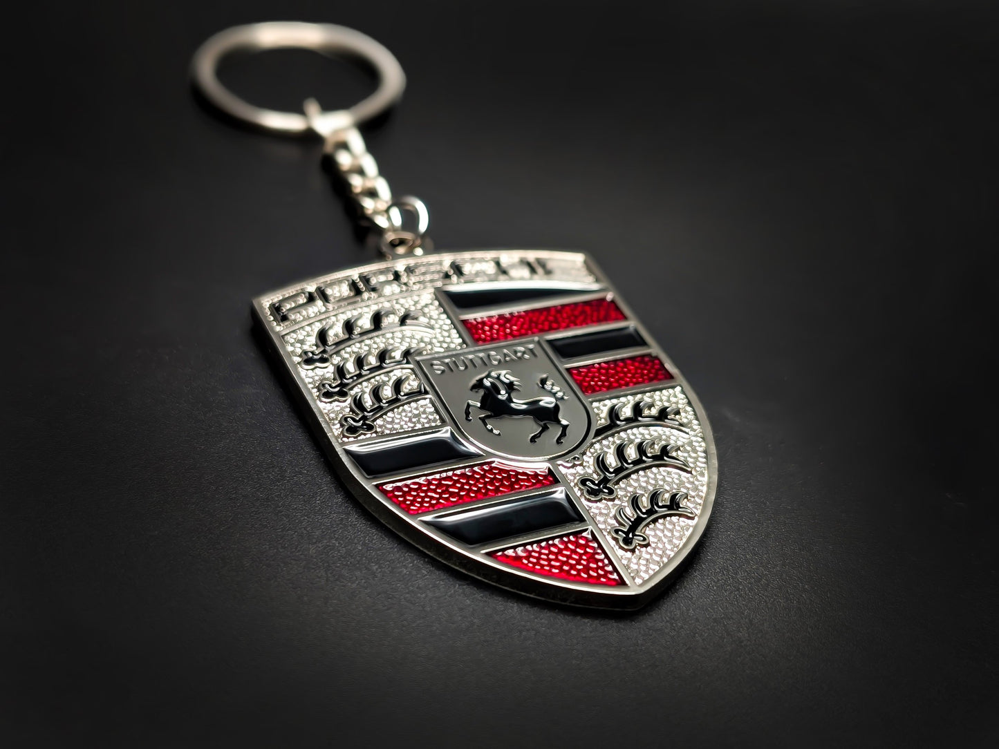 High-quality Porsche red crest keychain on a dark background, showcasing the polished silver trim and durable metal chain.