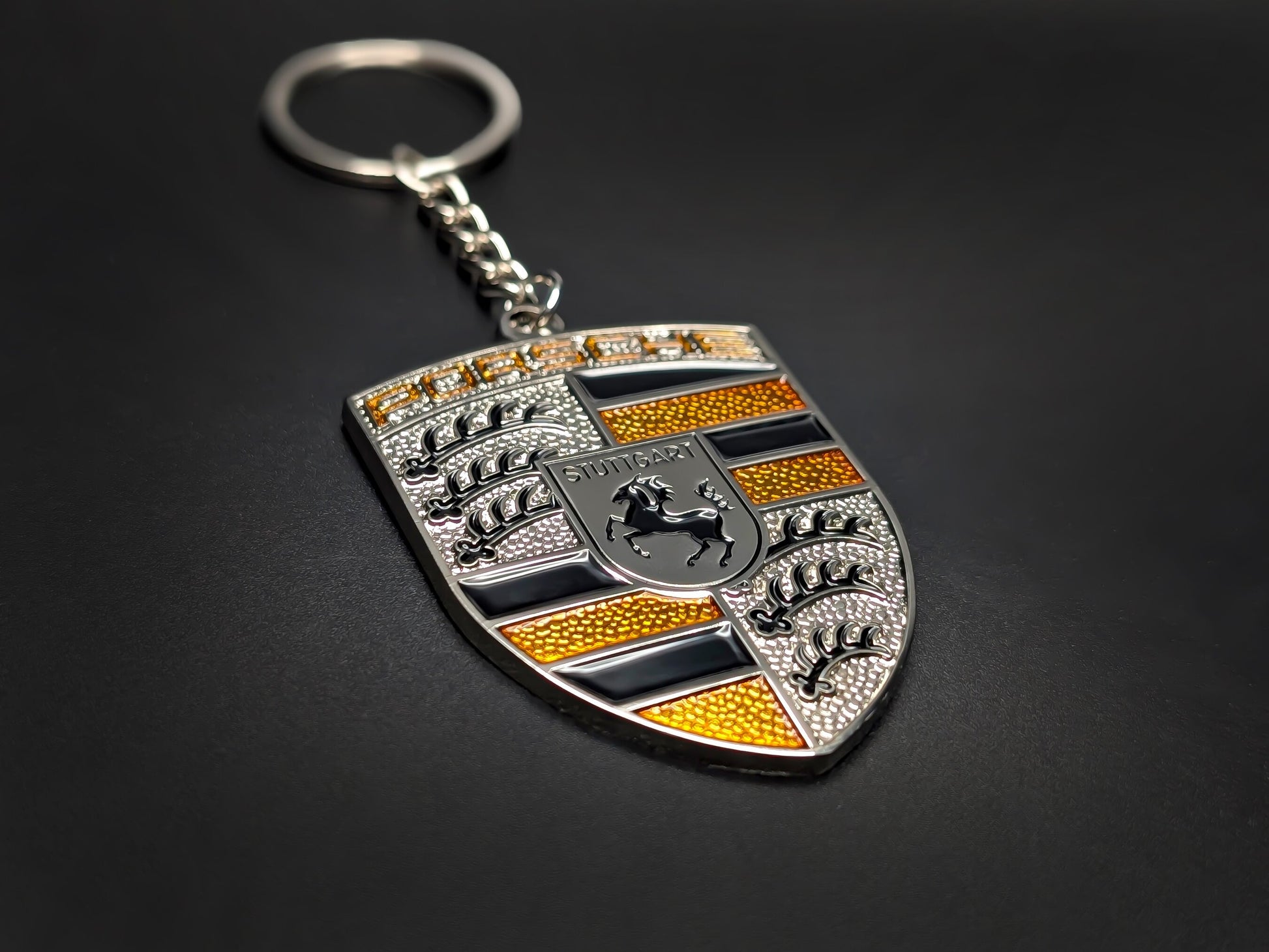 High-quality Porsche yellow crest keychain on a dark background, showing the polished silver trim and durable metal chain.