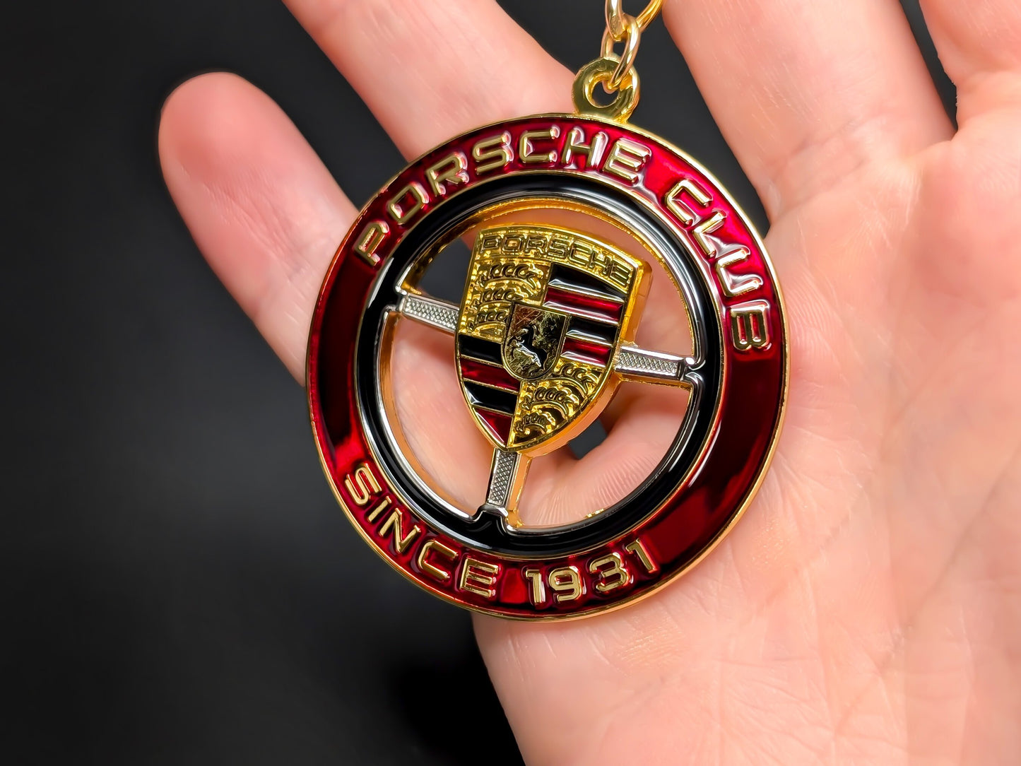 Standard size Porsche Club enamel badge keychain held in hand, displaying scale and metallic shine of the metal ring.
