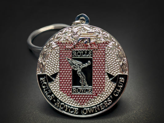 Close-up of a circular silver metal badge keychain featuring the Rolls-Royce Spirit of Ecstasy and Owners' Club crest.