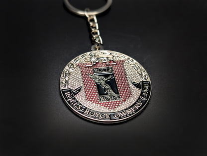 A Rolls-Royce Owners' Club badge keychain with a silver chain and ring, resting on a smooth dark background.