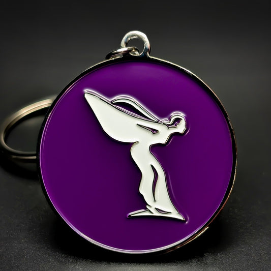 Double-sided metal Rolls-Royce badge keychain with a silver Spirit of Ecstasy figure in profile on a glossy purple enamel background, chrome split ring attached, on a dark studio surface.