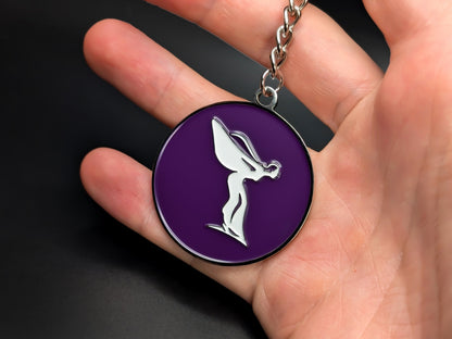 Hand holding a purple and silver Rolls-Royce Spirit of Ecstasy enamel keychain to show the 3D detail and premium metal finish.