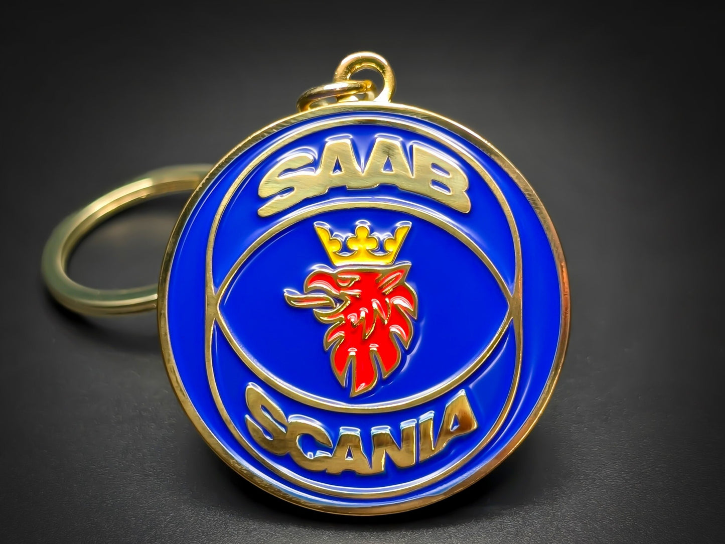 Premium Saab Scania badge keychain with gold-tone "Saab Scania" text and a red crowned griffin on a blue enamel background.