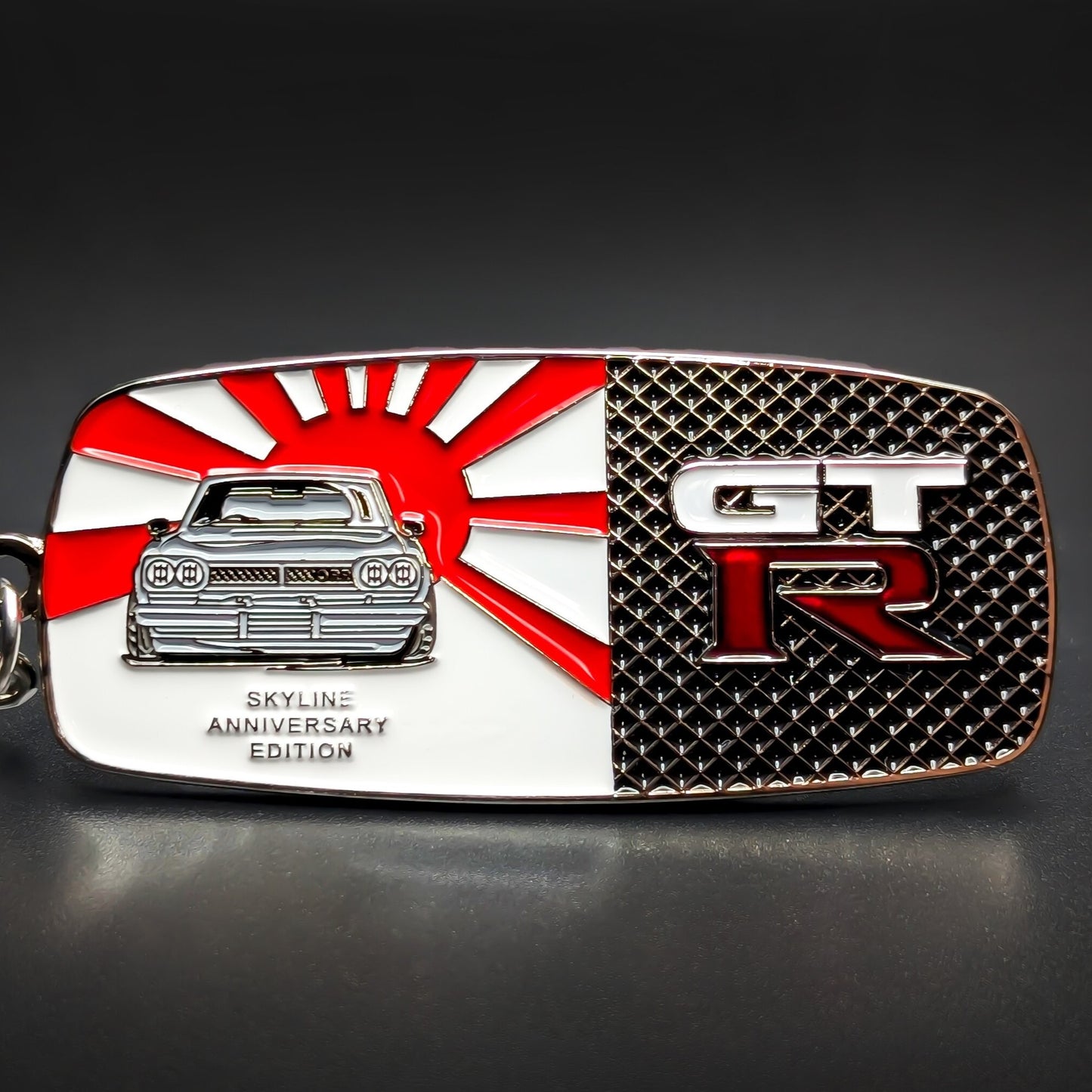 Double-sided rectangular metal Nissan Skyline GT-R badge keychain, left side a red-and-white rising sun with a silver Skyline car, right side black textured with white GT and red R lettering, chain and split ring.