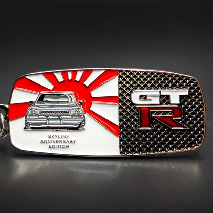 Double-sided rectangular metal Nissan Skyline GT-R badge keychain, left side a red-and-white rising sun with a silver Skyline car, right side black textured with white GT and red R lettering, chain and split ring.