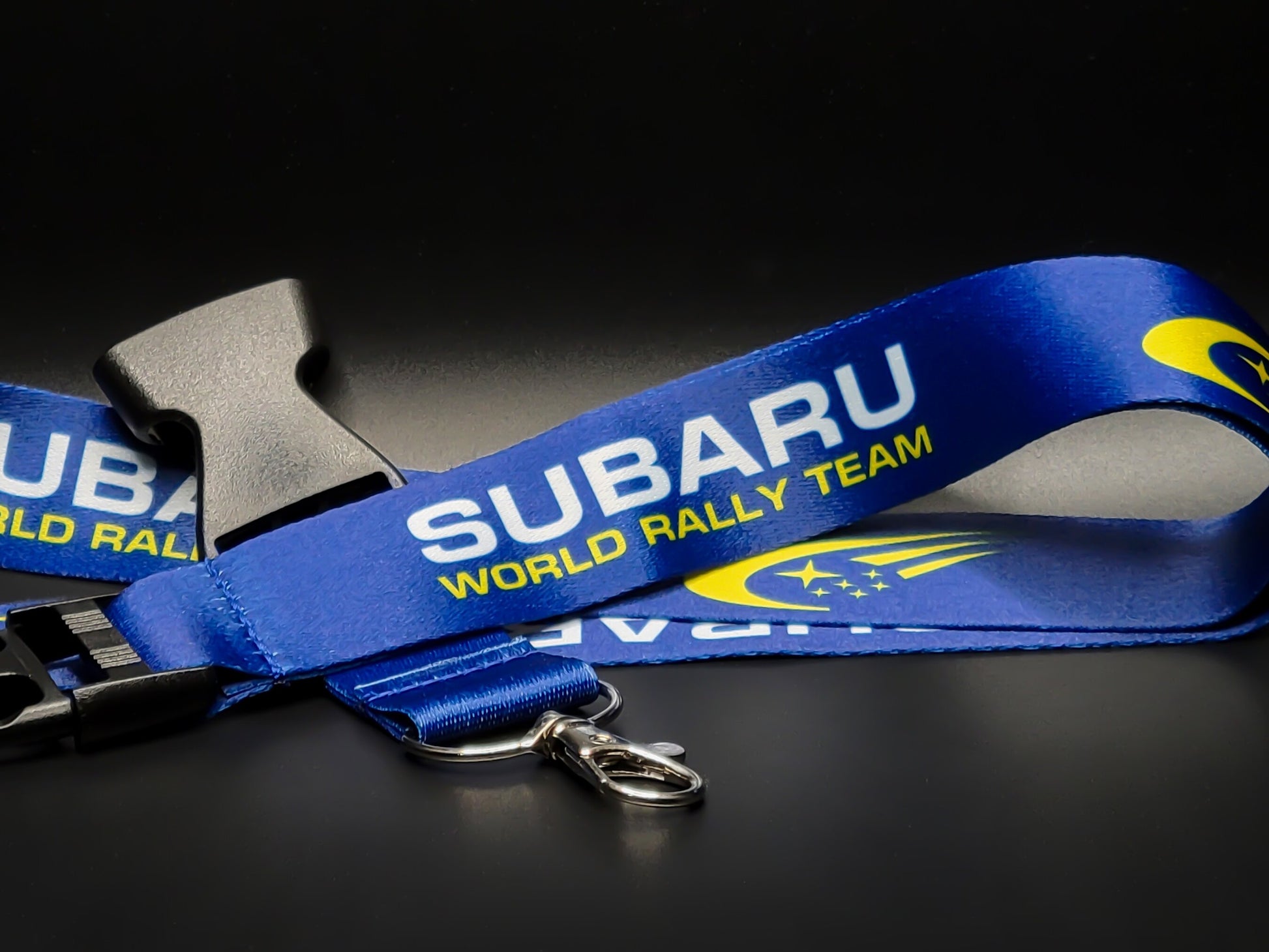 Blue Subaru World Rally Team lanyard with white and yellow text, featuring a black quick-release buckle and silver lobster claw clasp.