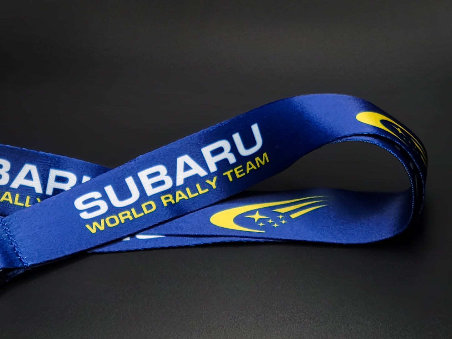 Close-up of a royal blue satin lanyard showing the Subaru World Rally Team wordmark and the iconic yellow star cluster comet logo.