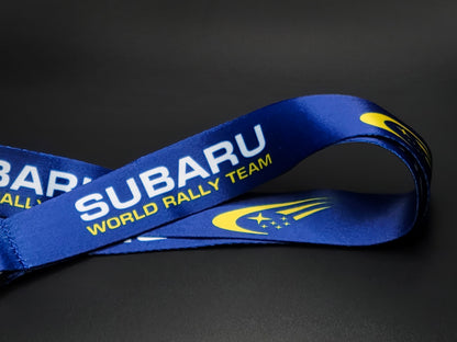 Close-up of a royal blue satin lanyard showing the Subaru World Rally Team wordmark and the iconic yellow star cluster comet logo.