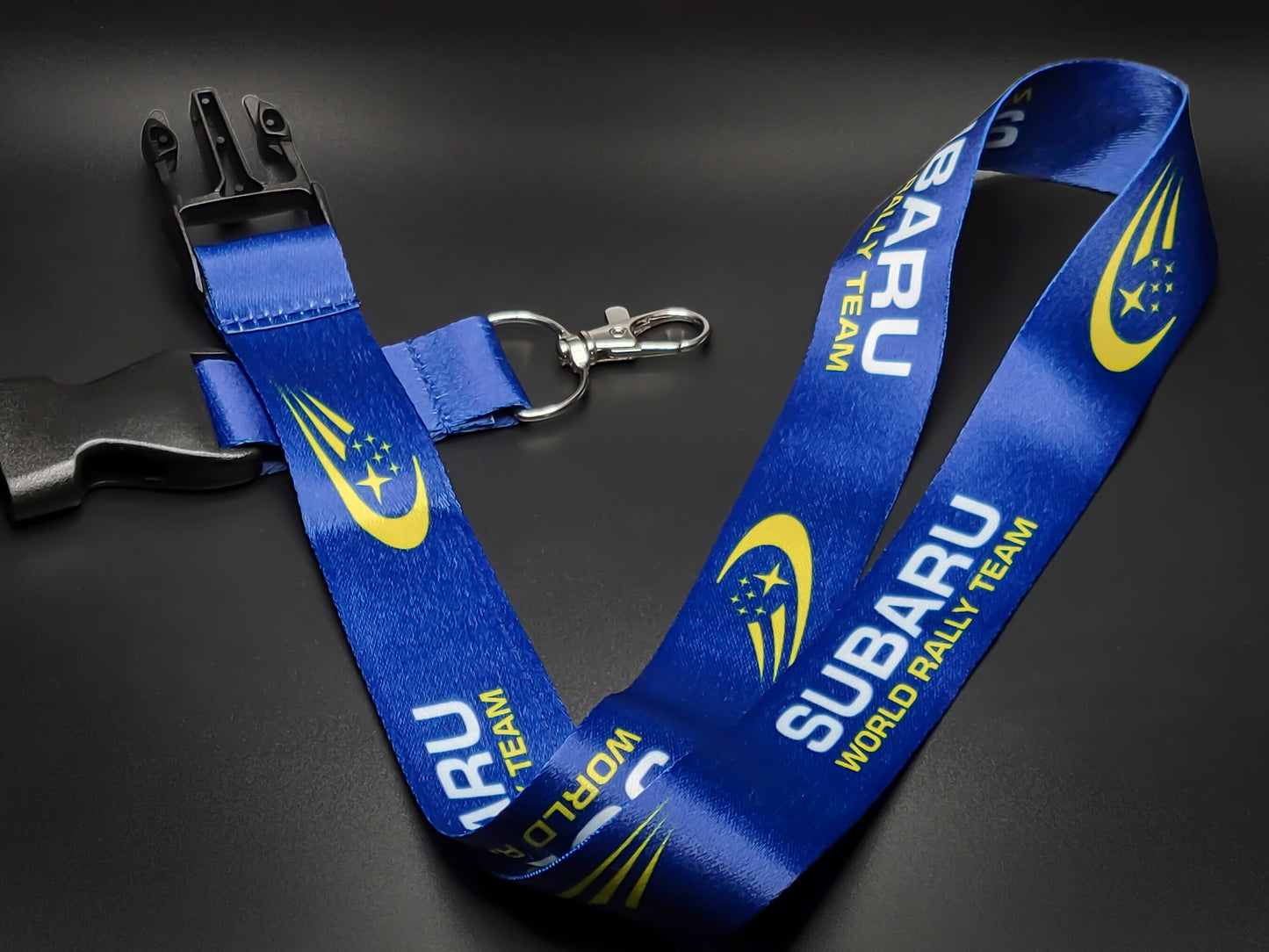 Full view of a Subaru motorsport lanyard laid out with its black plastic detachable buckle and durable metal key attachment.