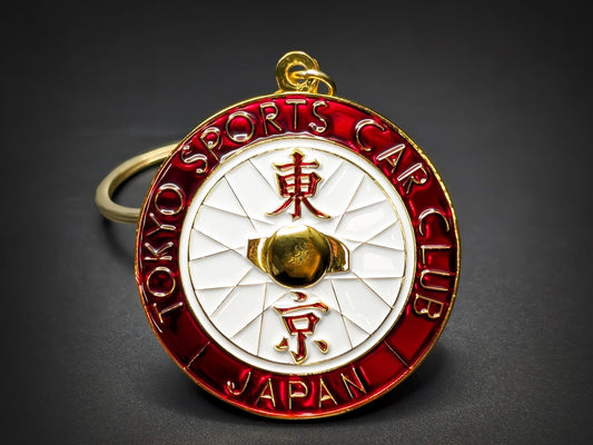 Tokyo Sports Car Club badge keychain with red enamel border, white spoke center, and gold Japanese kanji characters.