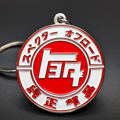 Double-sided metal Toyota JDM badge keychain, a red and white enamel medallion with Japanese lettering arched around the rim and a white emblem on the center disc, split ring, dark surface.