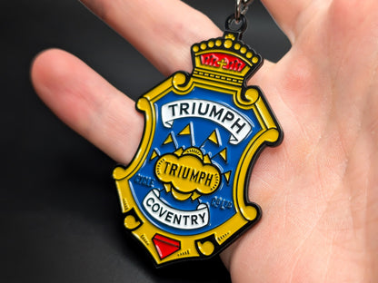 Hand holding a Triumph Coventry enamel badge keychain to demonstrate the size and premium 3D raised metal finish.