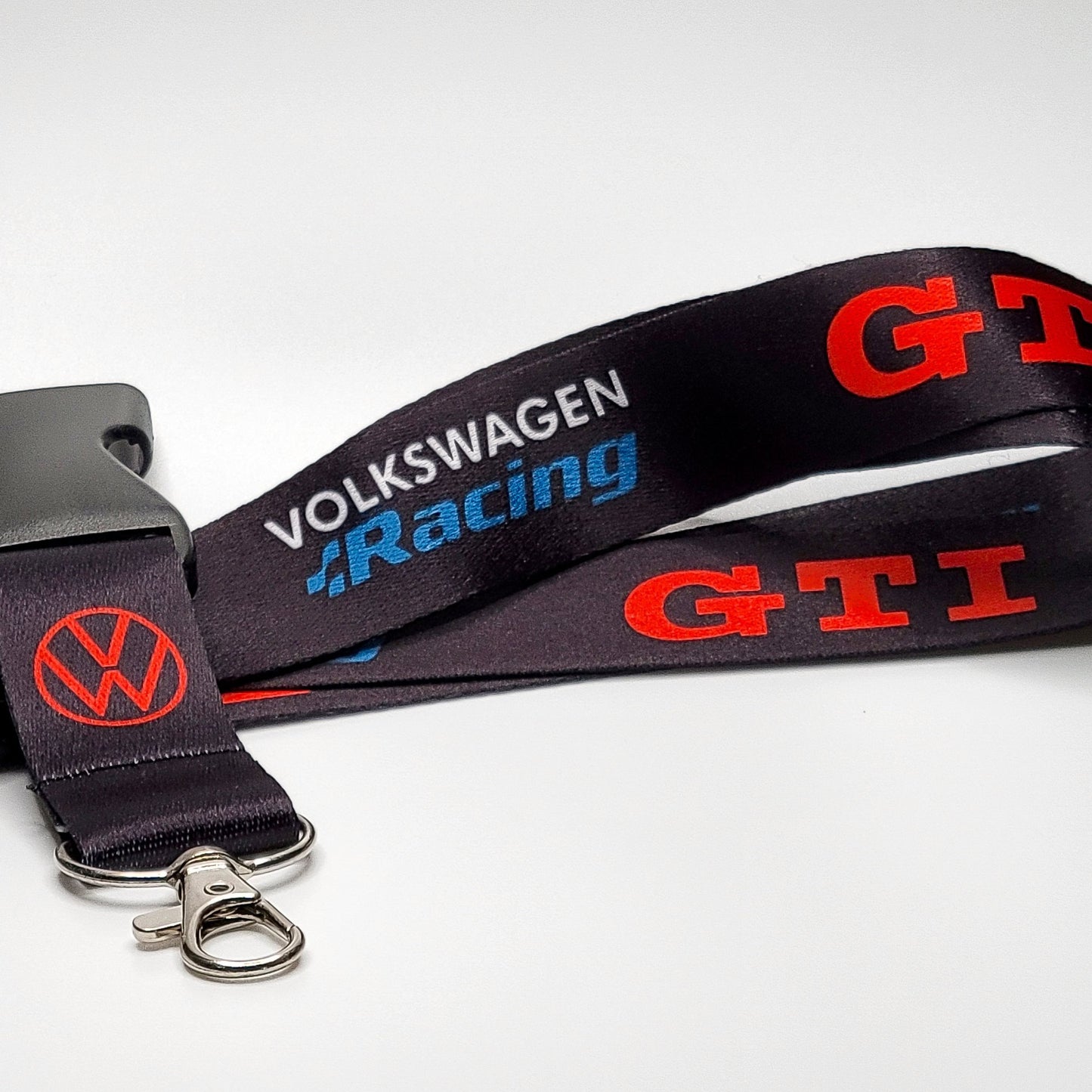 Black Volkswagen GTI lanyard with a red VW logo, white VOLKSWAGEN and blue Racing text, and bold red GTI lettering, coiled with a black breakaway clip and silver clasp on white.