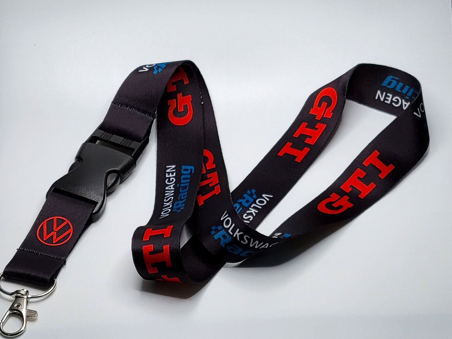 Premium black satin lanyard showcasing a repeating pattern of the red GTI logo, blue racing wordmark, and the red VW roundel.