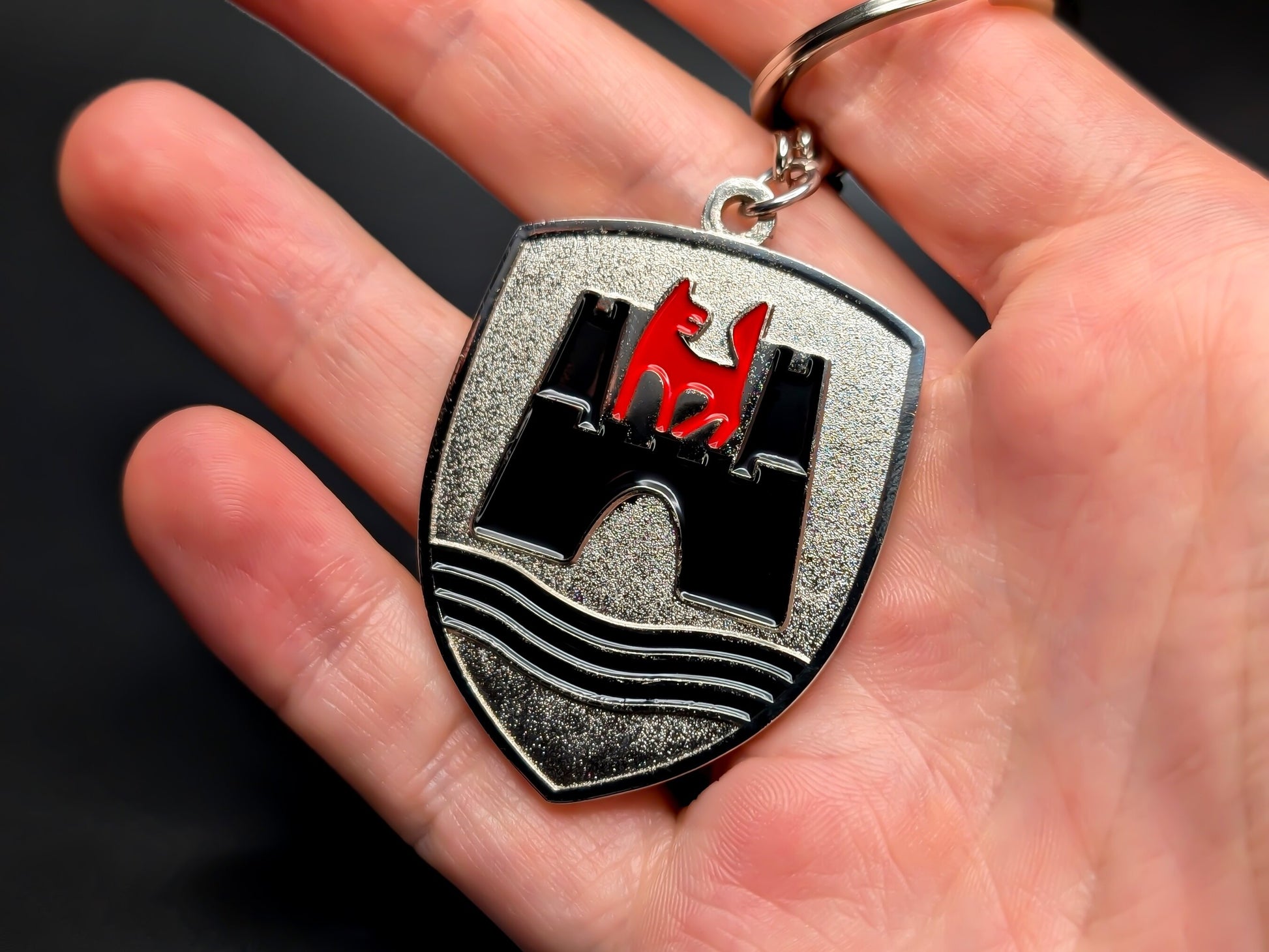 Hand holding a vintage-style Volkswagen Wolfsburg badge keychain to demonstrate scale and heavy-duty metal quality.